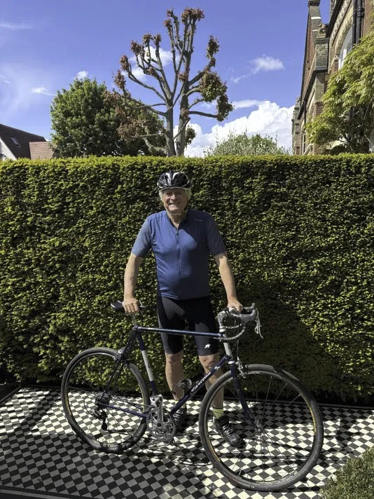 Nick Carr in cycling kit with a road bike, beside a hedge and a pollarded tree
