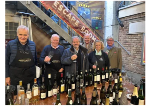 The Wine and Spirits Committee tasting, six people behind bottles under an Escape Room sign